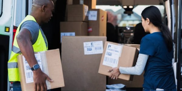 Two delivery people work together unloading packages from the back of a delivery van.